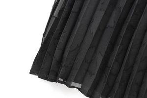 Détail d'une jupe midi plissée en mesh noir avec des motifs floraux en jacquard complexes