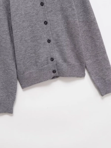Detail of grey knitted cardigan showing black buttons and ribbed hem texture