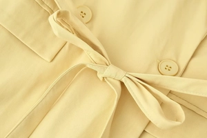 Detail of light yellow blazer jacket showing waist belt tie and twill fabric texture