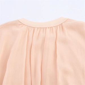 Detailed view of apricot chiffon dress featuring pleated round neckline and fabric texture