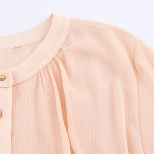 Detail of apricot pleated chiffon blouse featuring elegant gold buttons and stand collar