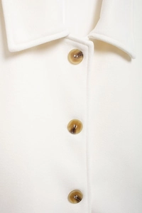 Détail d'un manteau en laine blanc avec revers élégant et boutons marron effet écaille