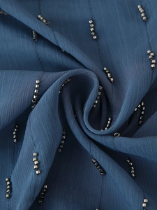 Macro shot of dark blue chiffon fabric with vertical silver beadwork and soft pleats