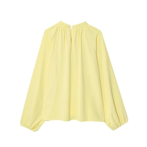 Detail of light yellow lantern sleeve blouse with high neck and delicate pleated texture