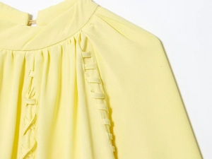 Detail of high collar with pleats and ladder trim on this pale yellow women blouse