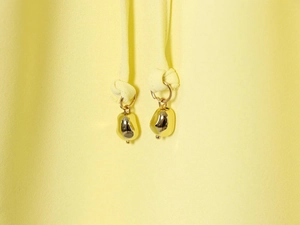 Macro detail of glossy gold metal teardrop pendants on yellow fabric drawstring