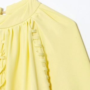 Pale yellow blouse with stand-up collar and pleated shoulders featuring woven trim details