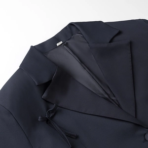 Detailed view of dark blue blazer with notch lapel and decorative bow accent on chest