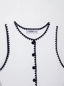 Close-up of white knitted vest with black scalloped trim and fabric covered buttons