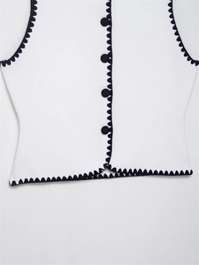Close-up of white knitted vest with black wave trim and round fabric-covered buttons