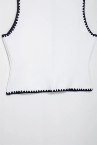 Detailed view of white knit vest with dark blue scalloped embroidered edges and texture