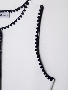 Detail of white knit vest collar with black scalloped edge and branded inner label