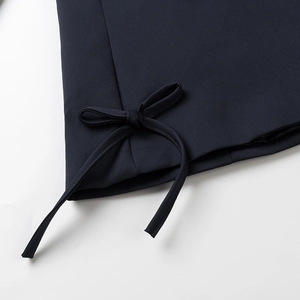 Detail shot of the dark blazer's bow tie decoration showing fine sewing and twill fabric texture