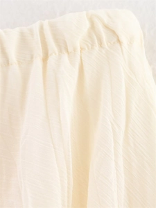 Detailed macro view of elastic waistband and pleated fabric on women's cream midi skirt
