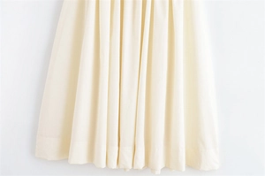 Detail shot of the cream-colored pleated skirt hem with sharp vertical fabric folds