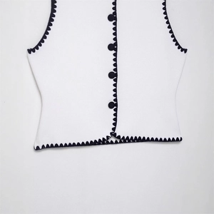 Close-up of white knit vest featuring contrast black scalloped edges and button details