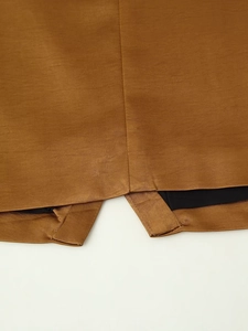 Detailed view of the tan satin fabric texture and adjustable buckle on the vest hem