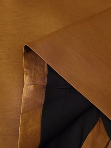 Macro detail of asymmetric vest showing silky bronze fabric and black lining textures