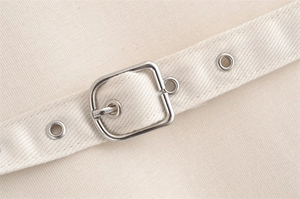 Detail of off-white twill belt with silver metal buckle and reinforced eyelets