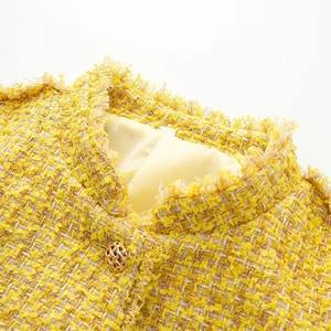 Macro detail of yellow tweed jacket with gold button and fringe trim neckline
