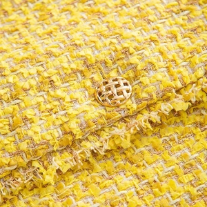 Macro detail of yellow tweed fabric with gold woven button on elegant women jacket