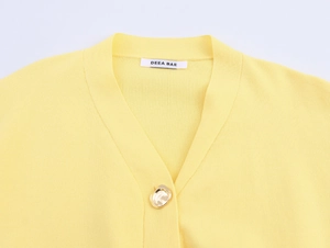 Detailed close-up of V-neck yellow knit cardigan with designer label and gold button