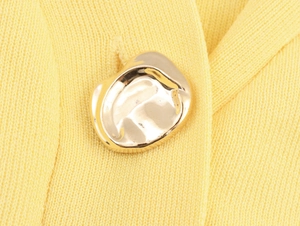 Macro shot of a textured golden metal button on yellow knit cardigan fabric