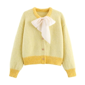 Detailed view of yellow knit cardigan featuring a large white silk bow and textured knit