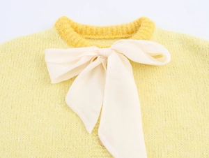 Macro view of bright yellow knitted cardigan with a large cream ribbon bow on the neckline