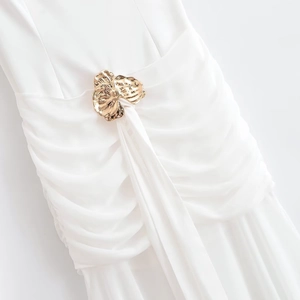 Close-up of elegant pleated waist detail with a golden flower metal buckle on a white dress