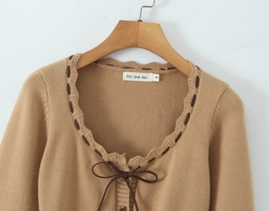 Dettaglio del cardigan in maglia color cammello con scollo a balze e chiusura a fiocco