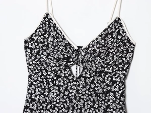 Detail of floral dress showing thin straps, V-neck white piping, and front lace-up cutout