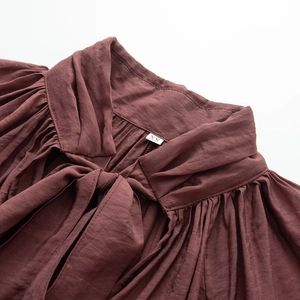 Close-up of the ruffled high neck and elegant self-tie bow on a dark red chiffon shirt