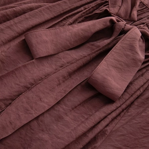 Detailed close-up of dark reddish-brown textured fabric with a stylish waist tie bow