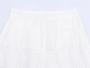 Dettaglio dei pantaloni bianchi con ricamo a occhielli geometrici e tasche laterali