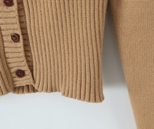 Dettaglio macro del cardigan in maglia cammello con trama a coste e bottoni scuri
