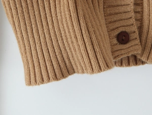 Dettaglio macro della maglia a coste e bottone marrone su cardigan beige