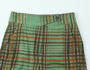 Close-up of green tartan plaid trousers featuring a single button waist and side pockets