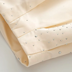 Macro detail of champagne satin jacket with shimmering rhinestone embellishments