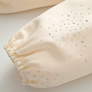 Close-up of cream satin sleeve cuff featuring sparkling rhinestones and elastic design