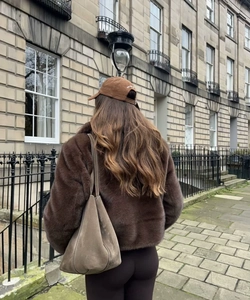 Detail einer braunen Kunstpelzjacke mit grauer Wildledertasche in urbaner Straßenkulisse