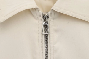 Close-up of the silver metal zipper and collar detail on a beige baseball jacket
