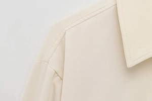 Macro detail of high-quality stitching on the collar and shoulder of the beige jacket