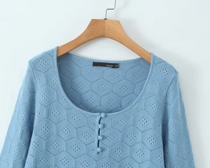 Detailed close-up of light blue knit sweater with hexagonal honeycomb texture and buttons