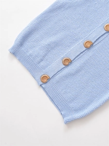 Detail of light blue knit top featuring golden snail-shaped buttons and textured fabric