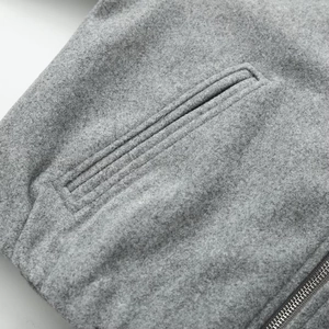 Detail of gray wool jacket featuring refined pocket stitching and metallic zipper texture