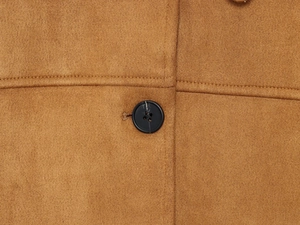 Détail de la texture en daim marron et du bouton noir avec des coutures doubles impeccables