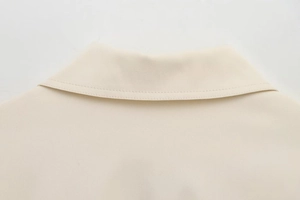 Detail of beige jacket collar showing fine stitching on woven fabric with lapel