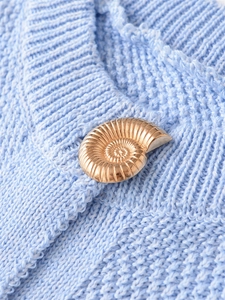 Detail of light blue knit vest featuring a gold seashell-shaped metal button closure