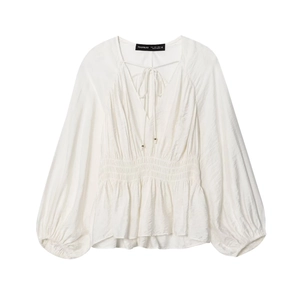 Detail of white V-neck blouse featuring smocked waist and delicate tie neck design